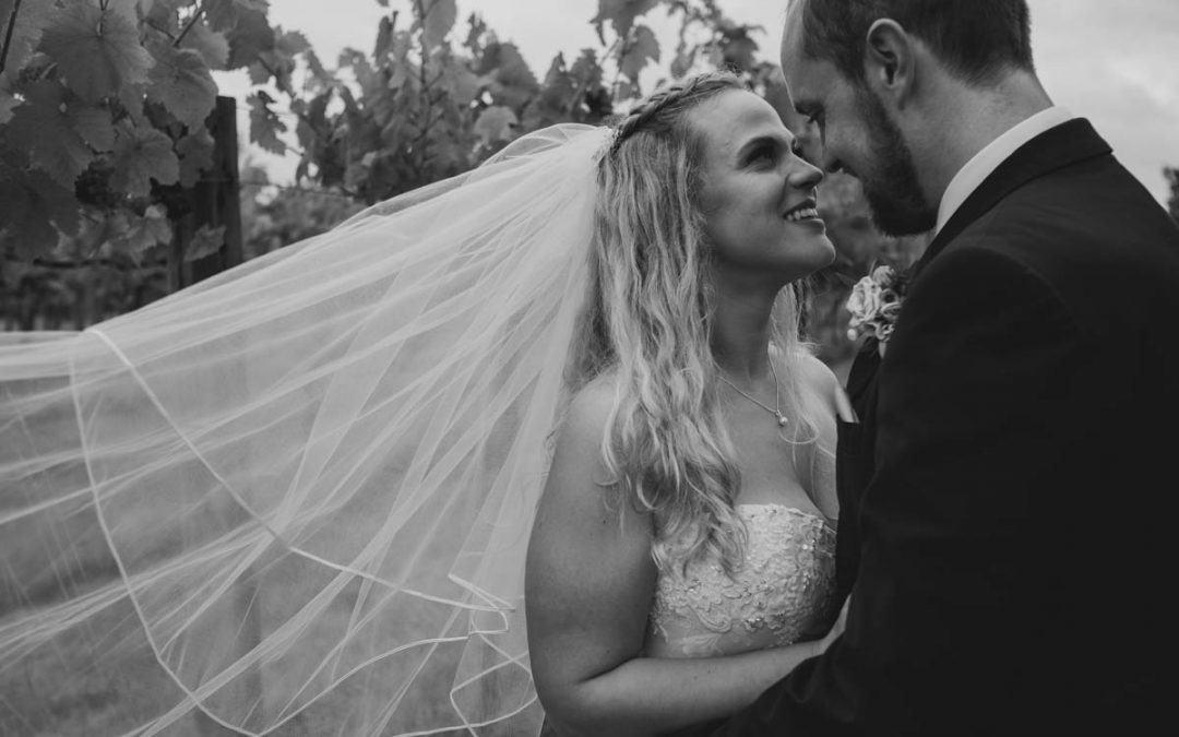 brides veil blows in the wind while she cuddles her groom