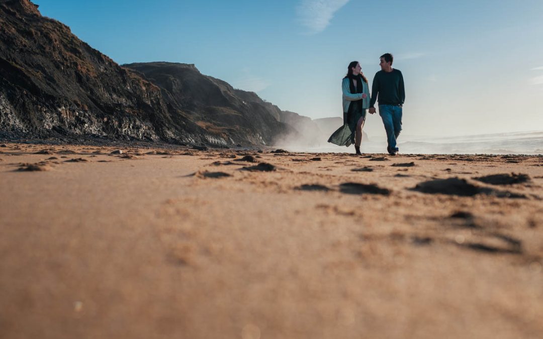 engaged couple walk hand in hand along charmouth beach