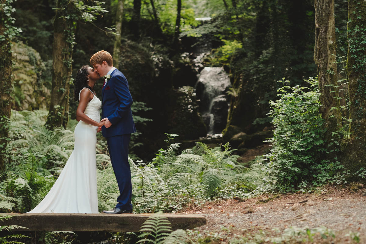 groom kisses his wife in front of the waterfall at canonteign