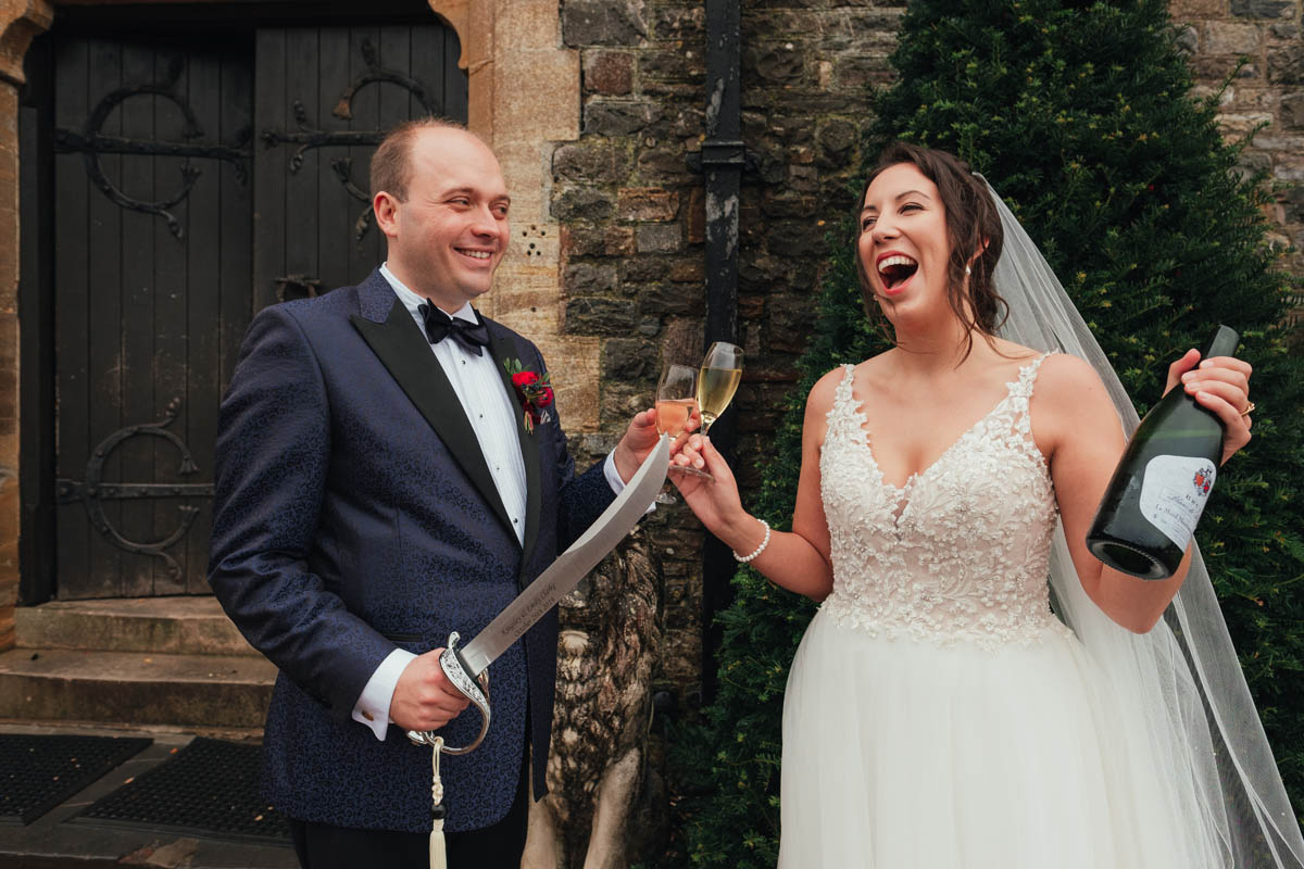 bride and groom laughing with champagne and sword