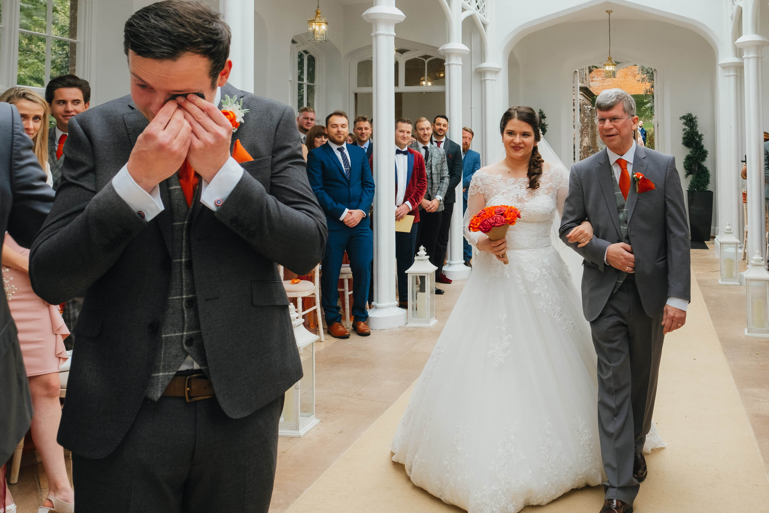 a groom wipes away a tear as the bride's father walks her down the aisle