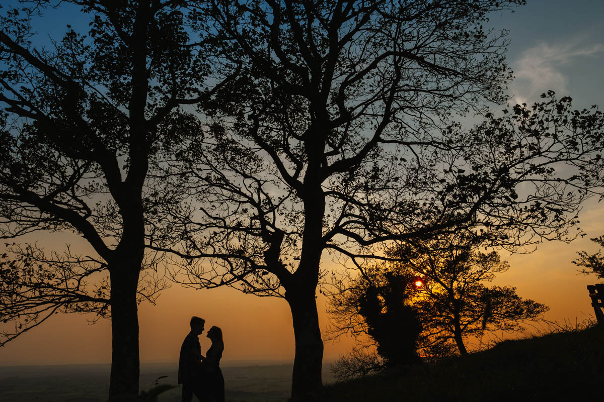 a couple kiss beneath the trees as sunset on their engagement shoot