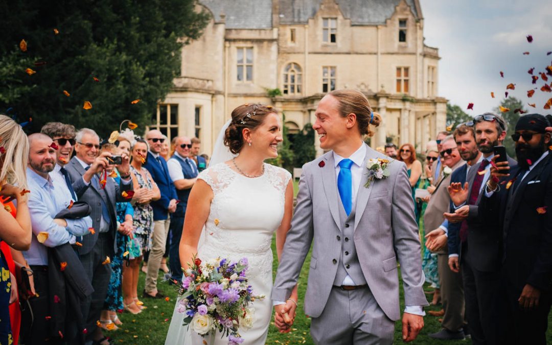the couple walk down an aisle while guests throw confetti at their orchardleigh wedding