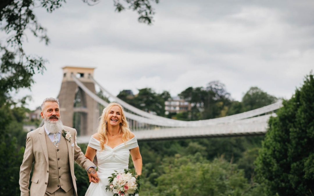 bride and groom smiling walking towards the camera with Clifton suspension bridge in the background
