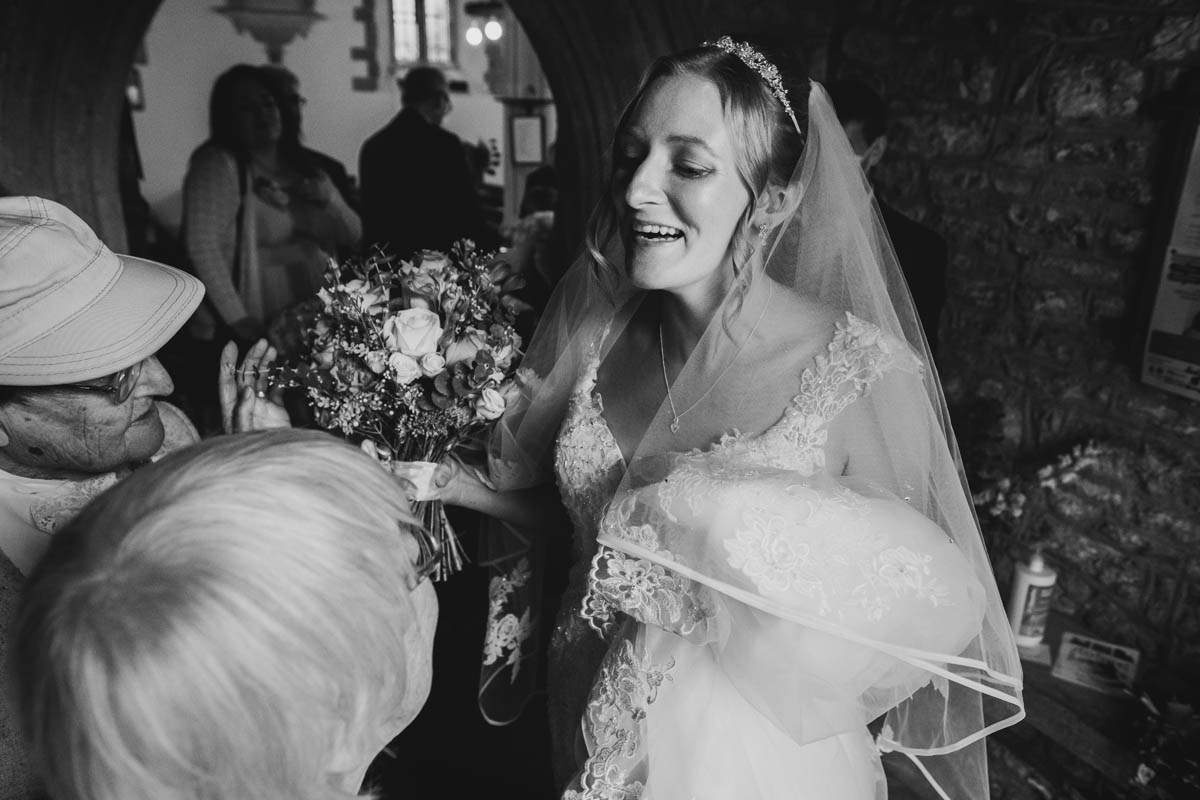 the bride laughs as she shelters from the rain in the church porch