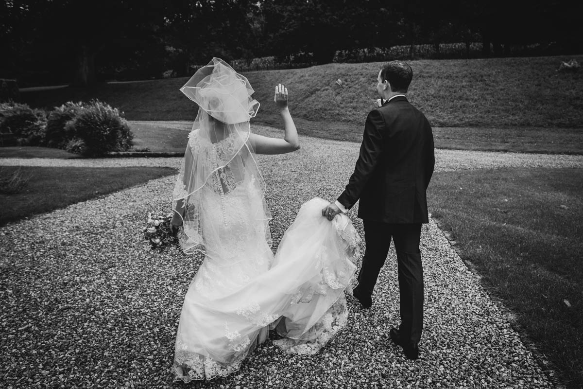 the bride's veil blows in the wind and the groom holds her wedding dress train in blagdon
