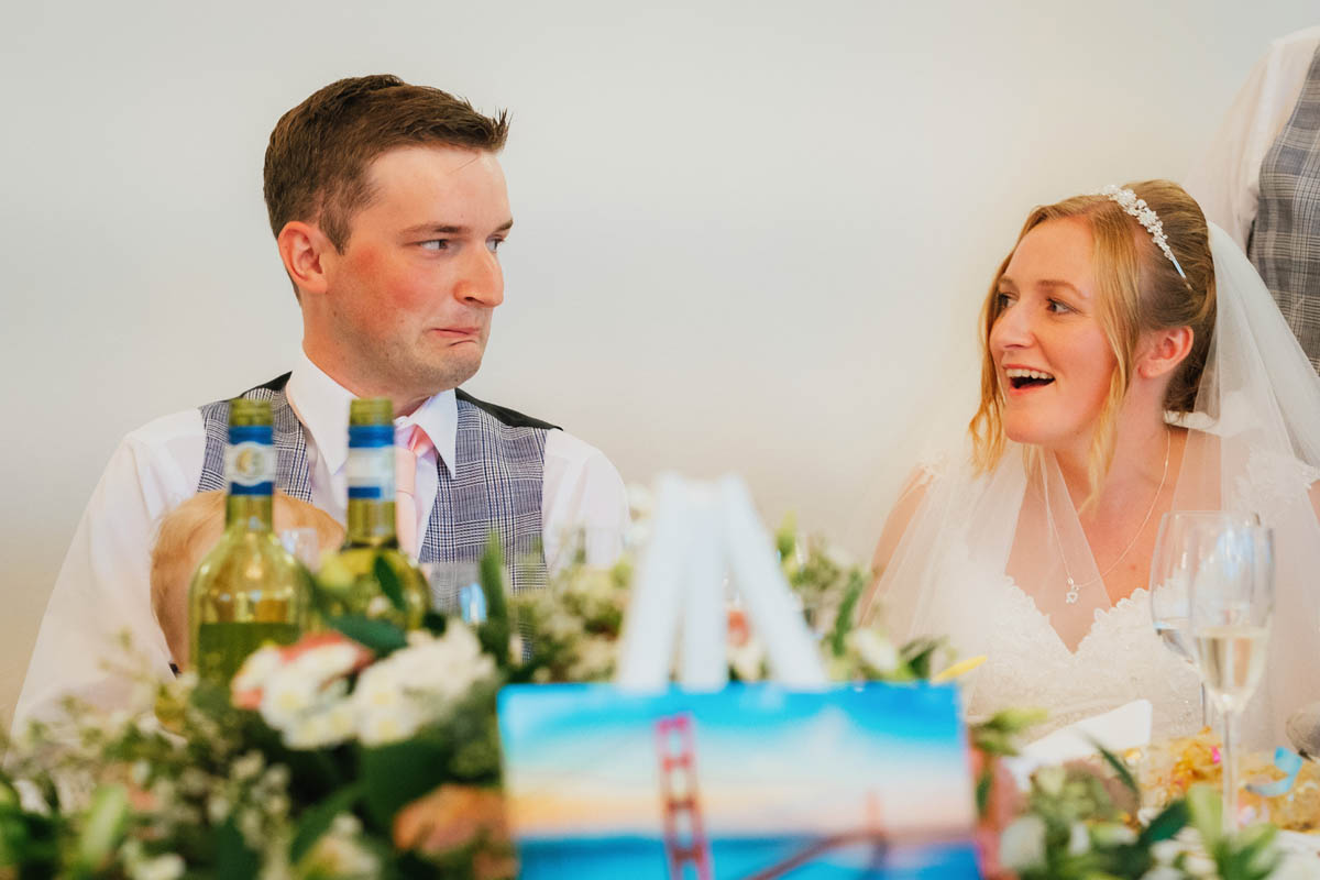 the groom looks awkward and the bride laughs during the father of the bride's speech