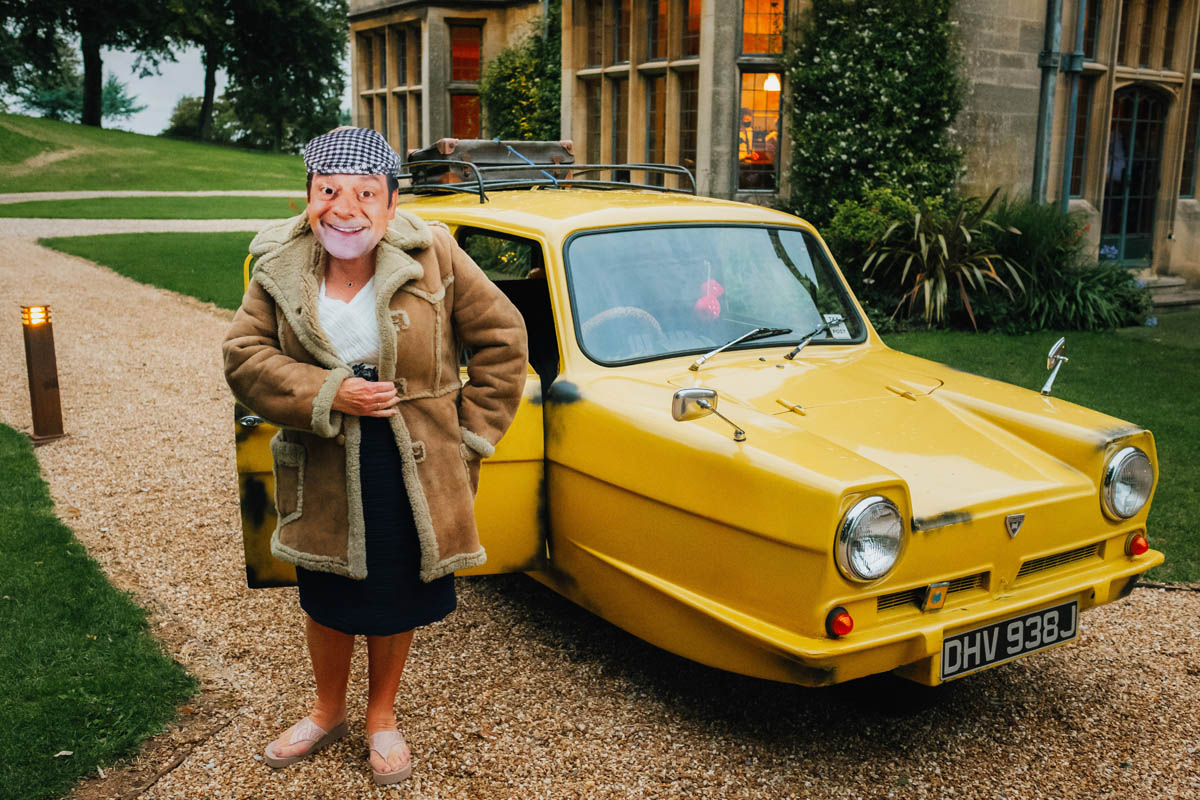 mother of the bride dressed up as Del Boy with a yellow three wheeled car in the background