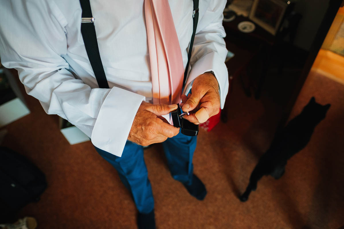 father of the bride putting on his cufflinks, a cat wonders in the background