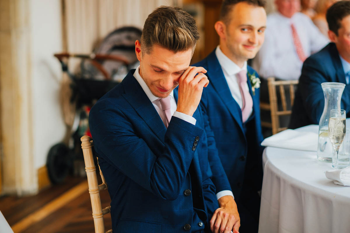 the bride's brother cries as his partner looks on knowingly behind
