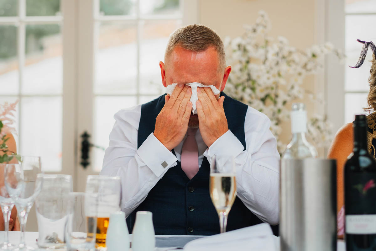 the father of the bride hangs his head into a tissue as he cries after his wedding speech
