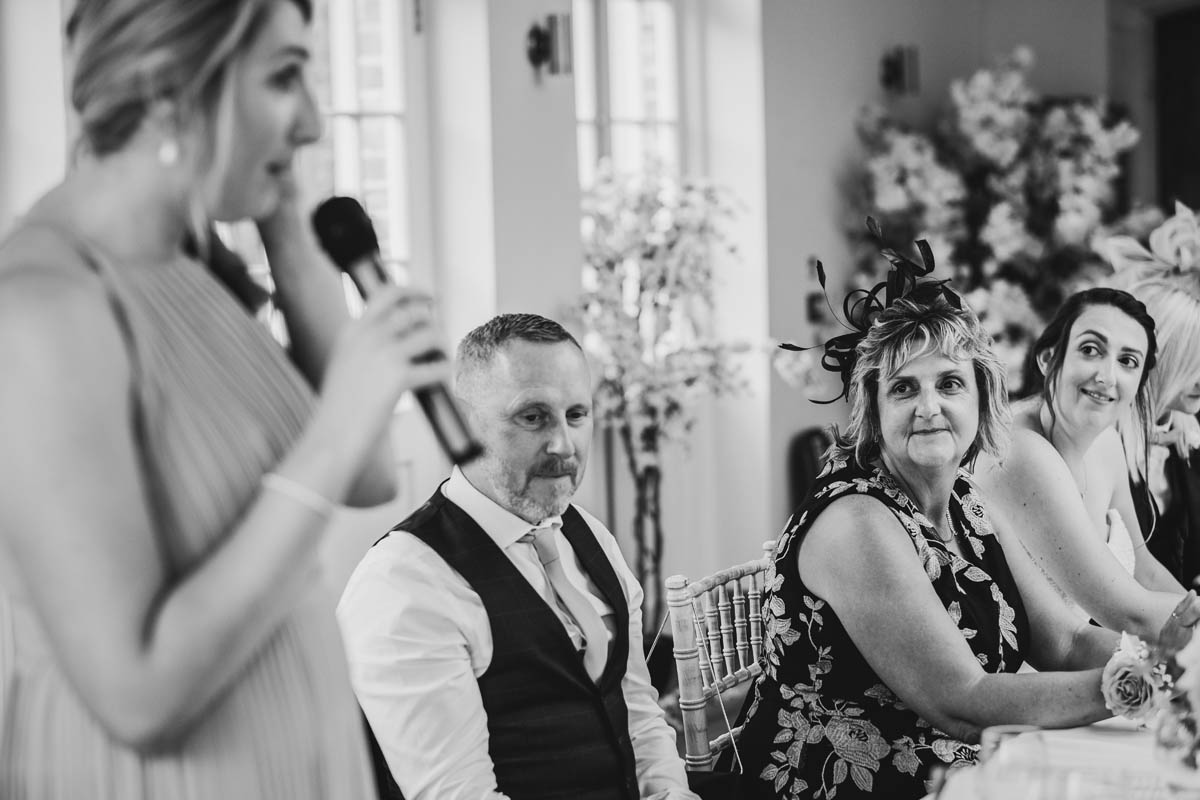 the bride's mother looks on in pride as her daughter gives her wedding speech