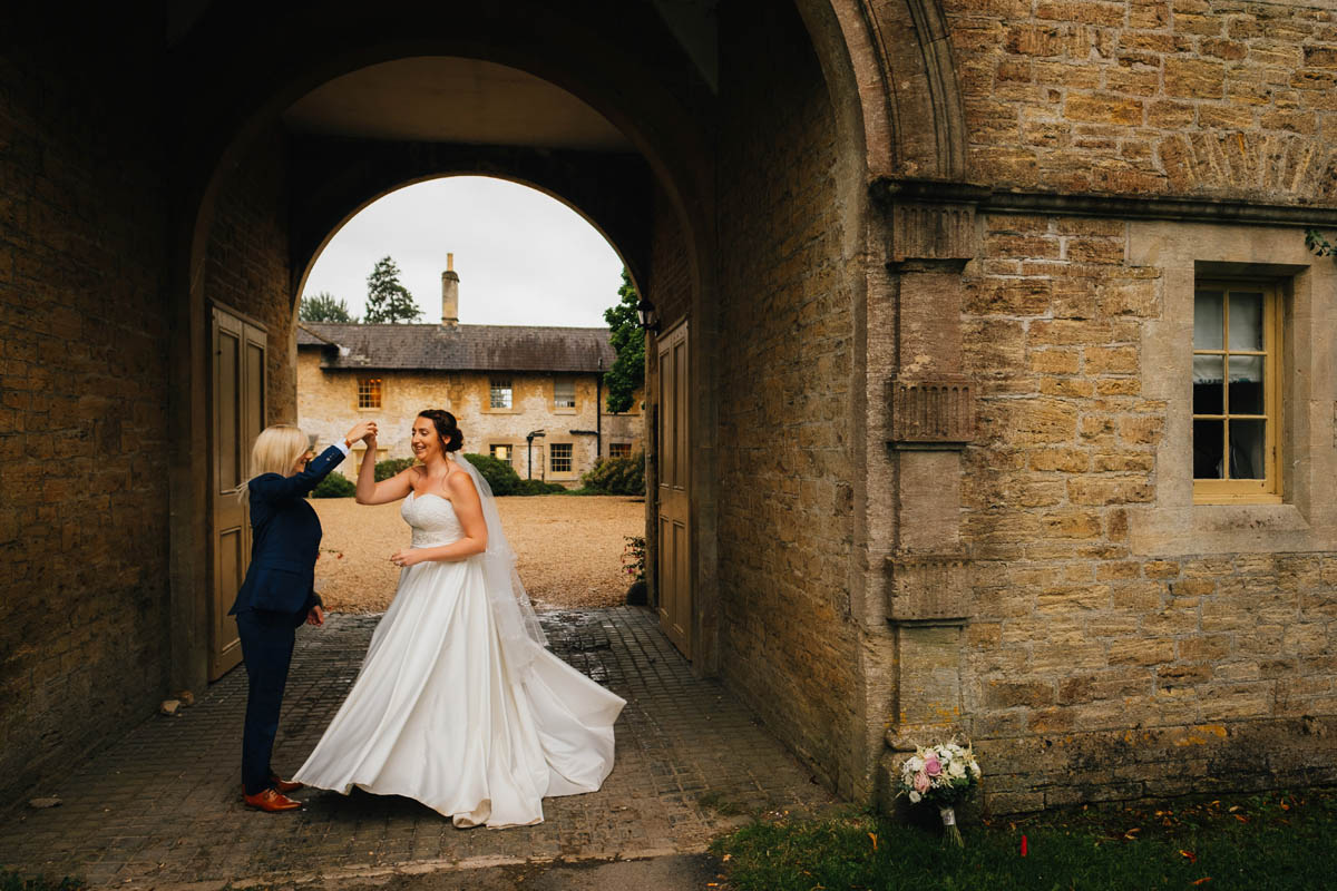 the bride swings her new wife around in a dance under the archway on the Orchardleigh estate