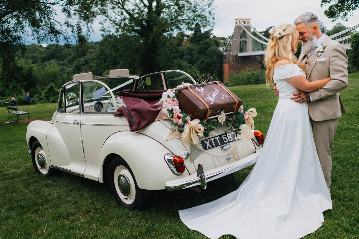bride and groom hug in front of the Clifton suspension bride with a Morris Minor in the background