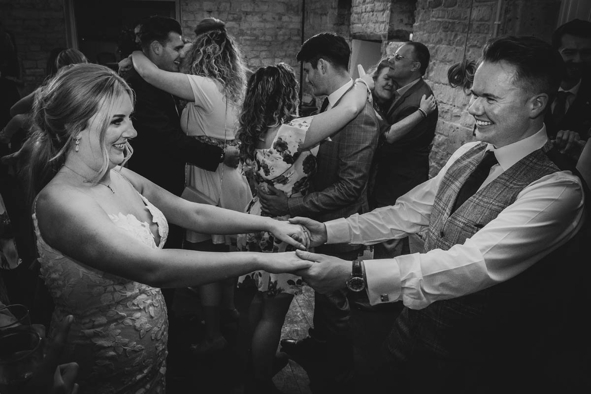 black and white photograph of the newly weds dancing, they fold hands and smile at each other