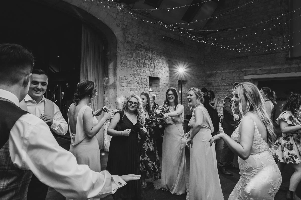 black and white photograph of guests dancing at Lapstone barn, fairy lights adorn the ceiling