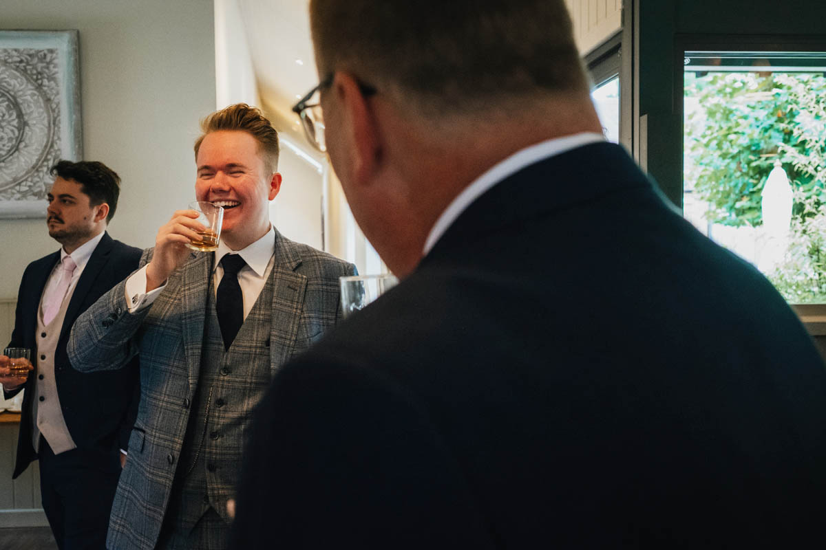the groom drinks whisky and laughs with his groomsmen