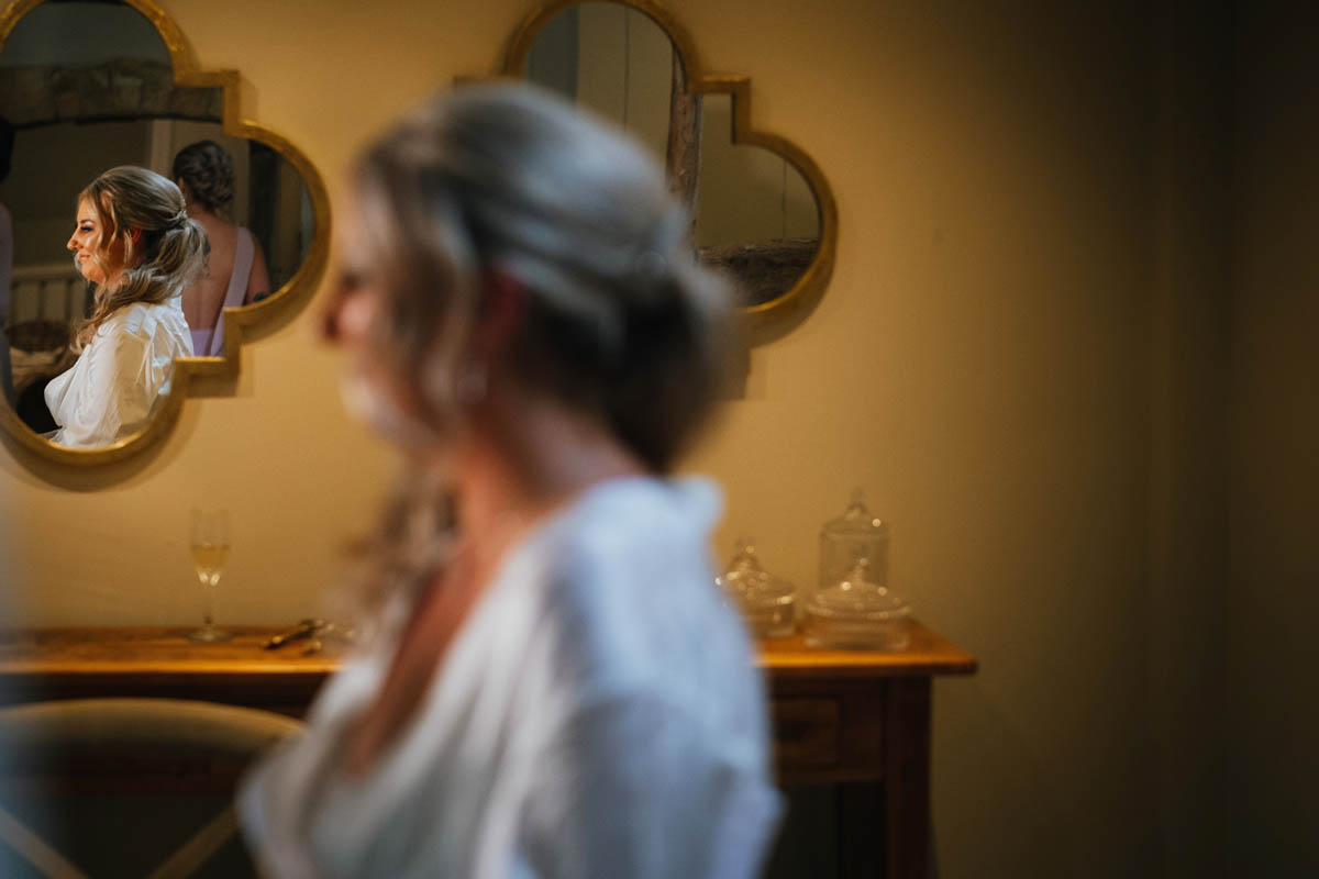 a reflection of the bride in the mirror as she has her wedding make-up put on by a make-up artist