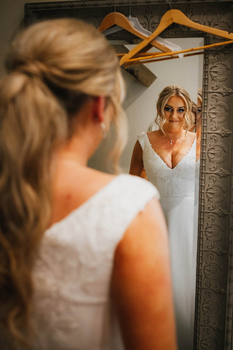 the bride looks at herself in her wedding gown in the mirror