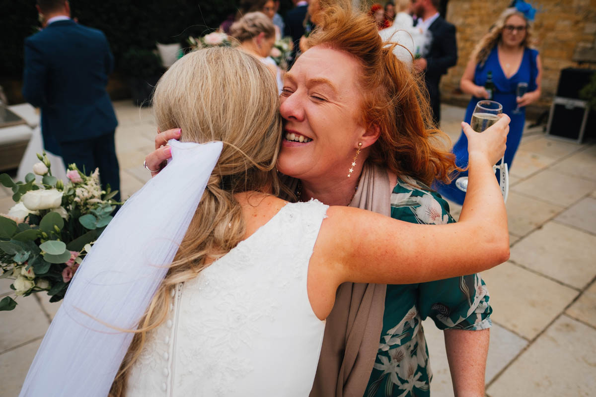 a woman grins as she gives the bride a hug
