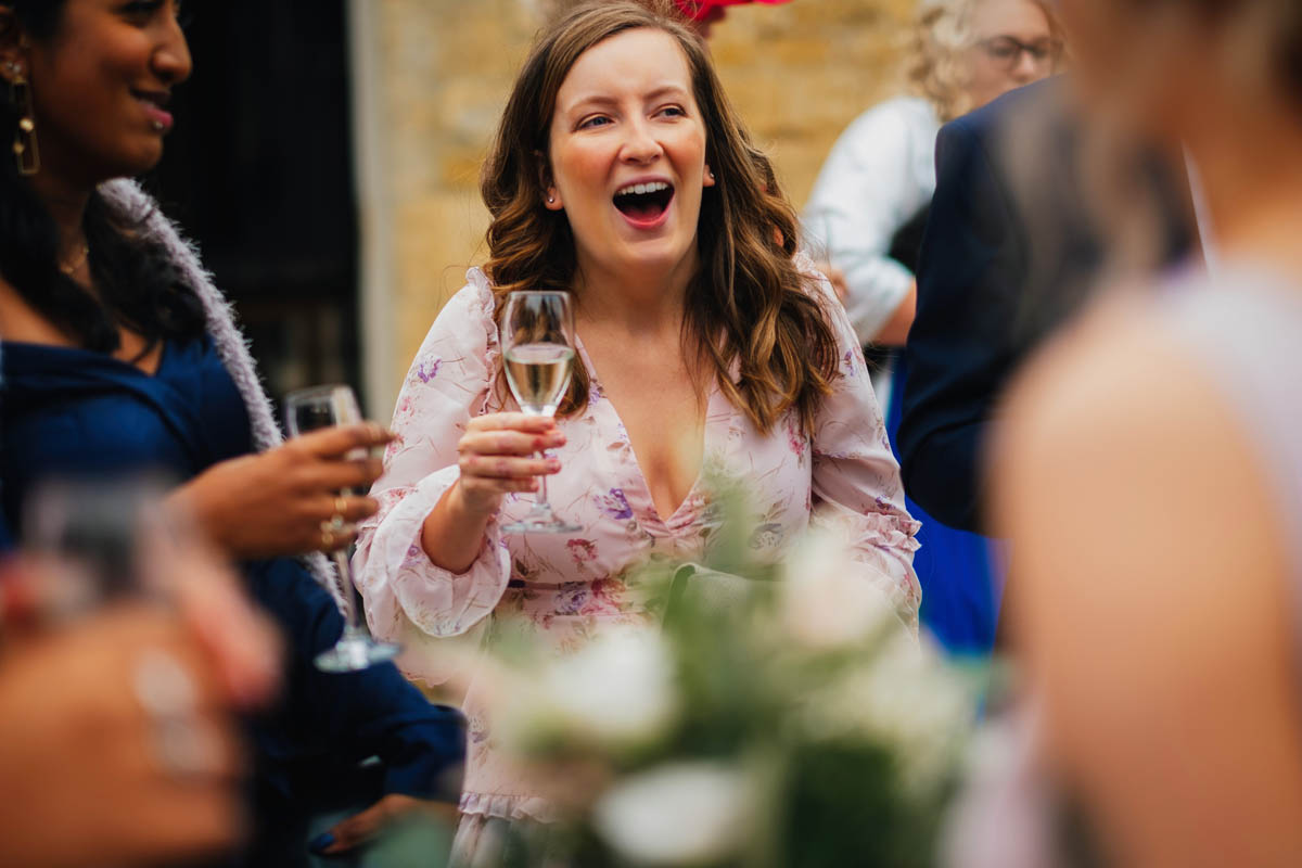a wedding guest laughs while she drinks her champagne