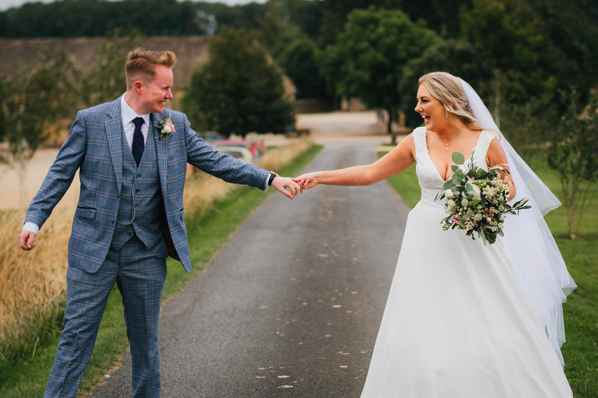 the newly weds walk apart and hold hands whilst laughing at each other as they walk up the drive of Lapstone barn