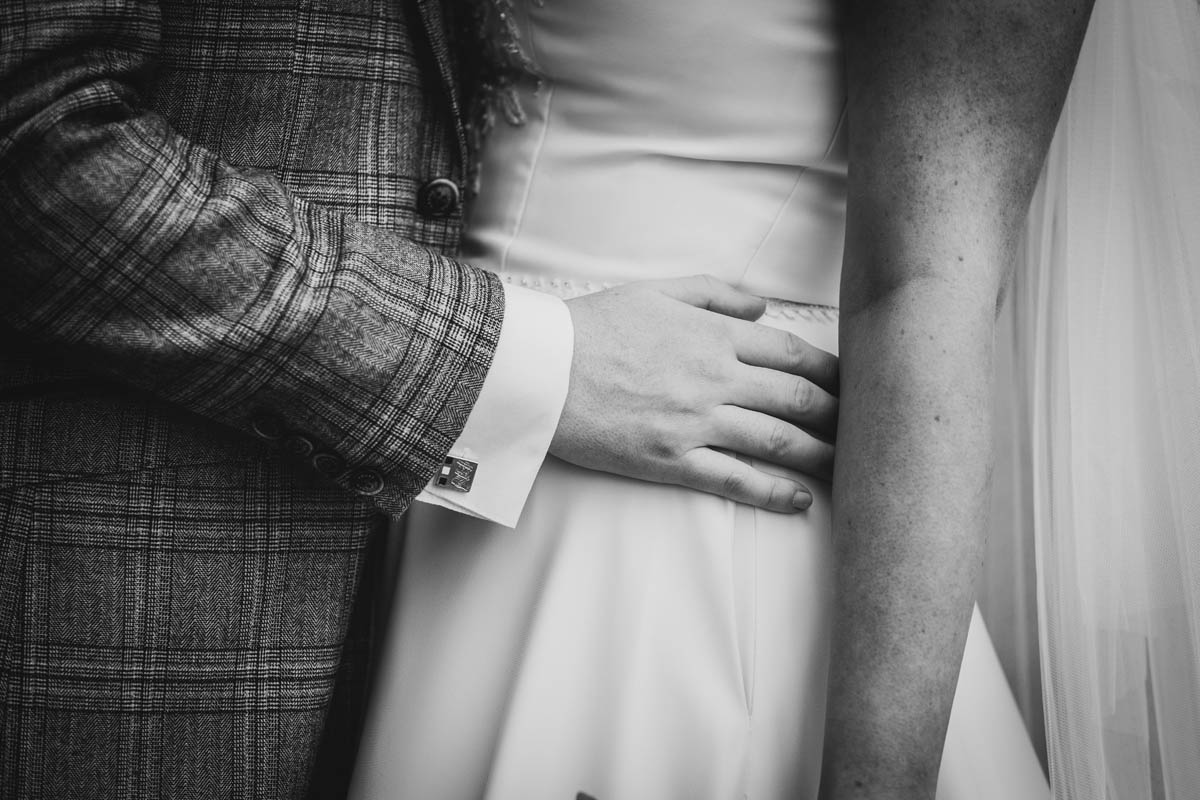 a close up of the man's hand holding his wife's waist in her wedding dress