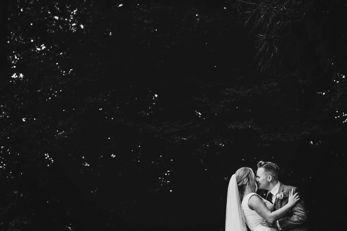 blacka nd white photograph of trees behind the groom kissing his new wife