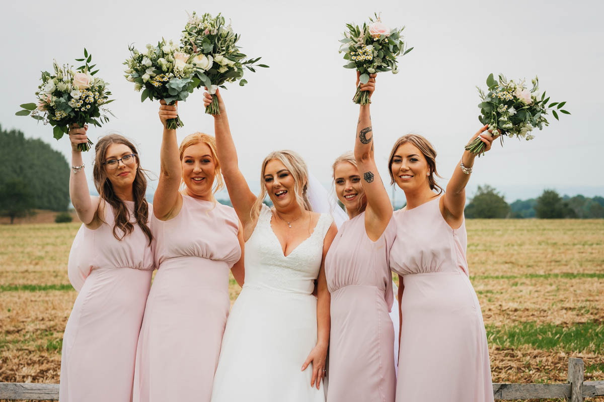 the bride and her bridal party raise their bouquet into the air