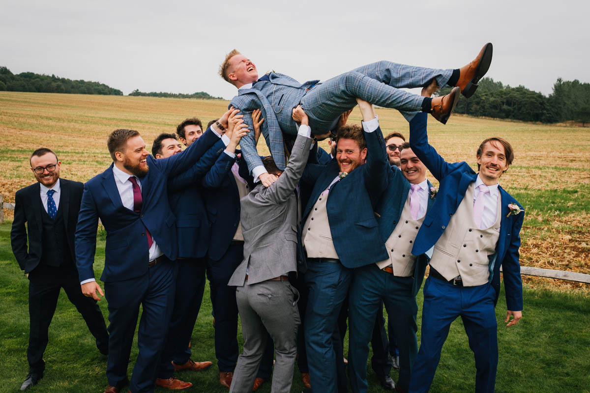 groomsmen lifting the groom into the air while he laughs