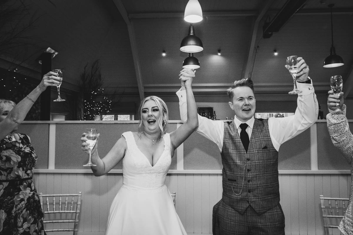 the new married couple hold their hands in the air and cheers on the top table