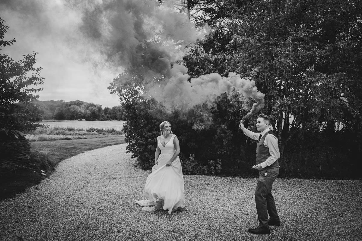 black and white photograph outside Lapstone barn of a newly-wed couple waving a smoke bomb