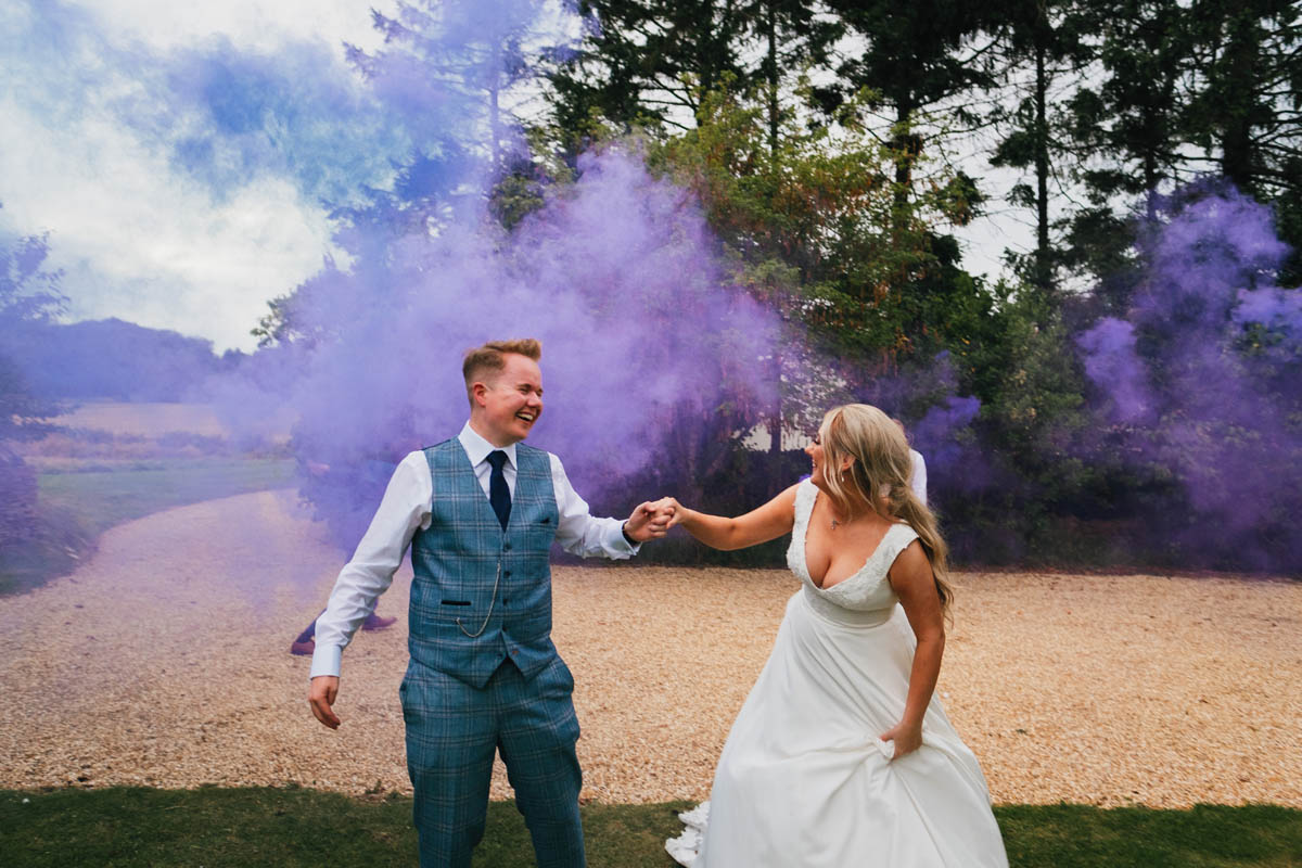 the new mr and mrs laugh whilst purple smoke is behind them