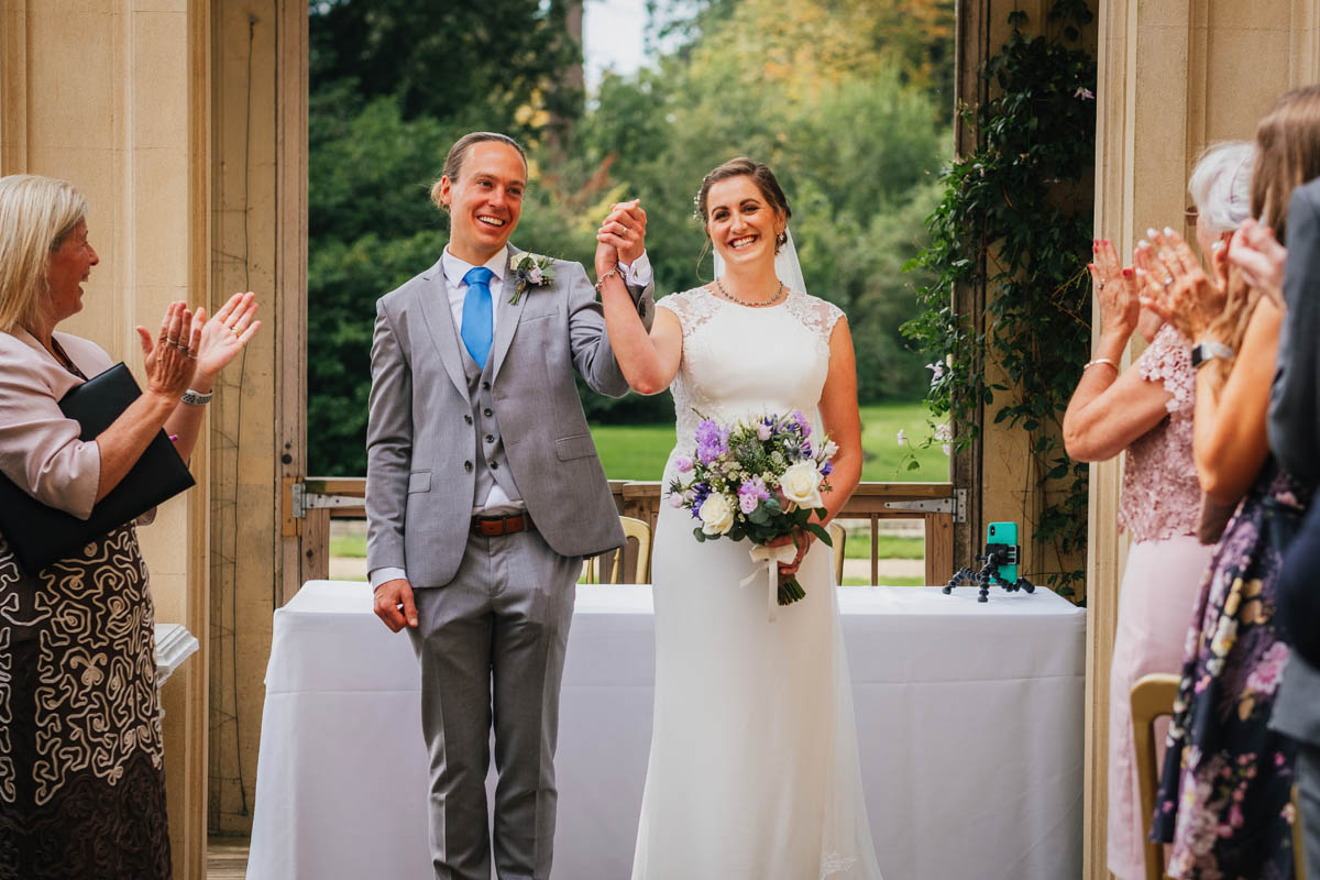 the couple raise their hands in joy while wedding guests clap as they depart from their wedding ceremony