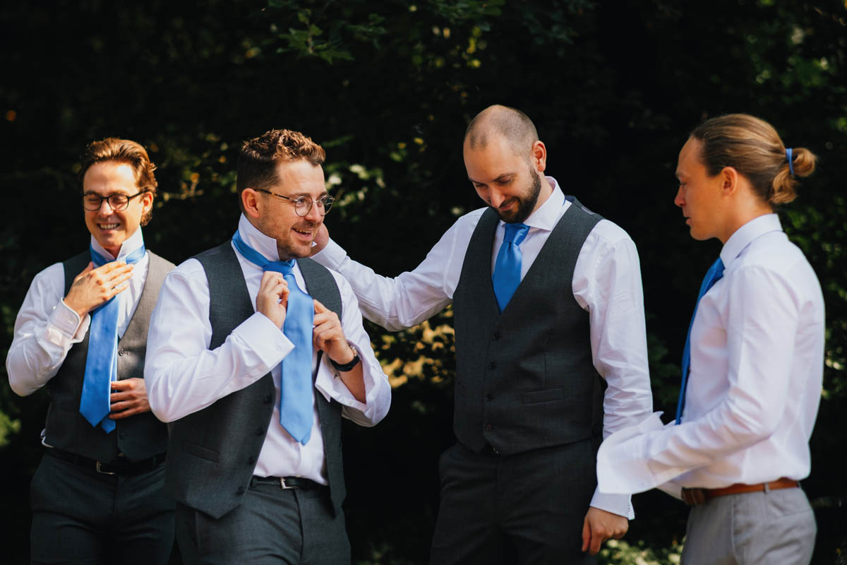 four white groomsmen smile and tie their ties