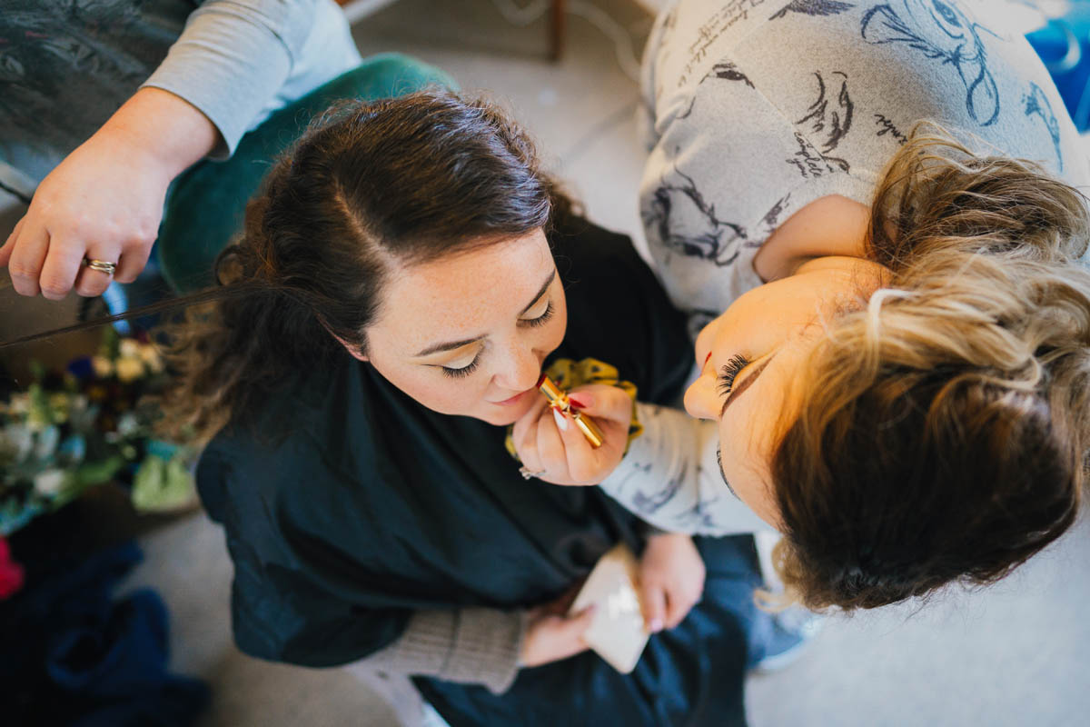 a shot from above of the bride having her lipstick applied by her sister-in-law