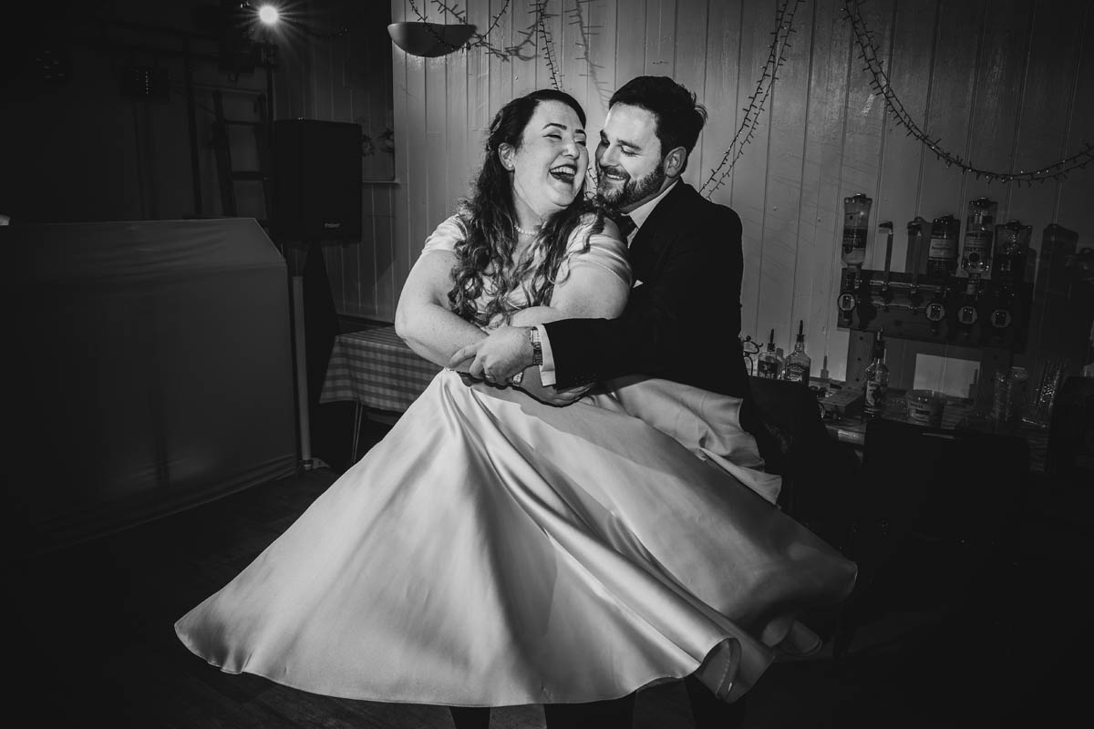 the bride and groom laugh as he spins her around the dancefloor, in monochrome