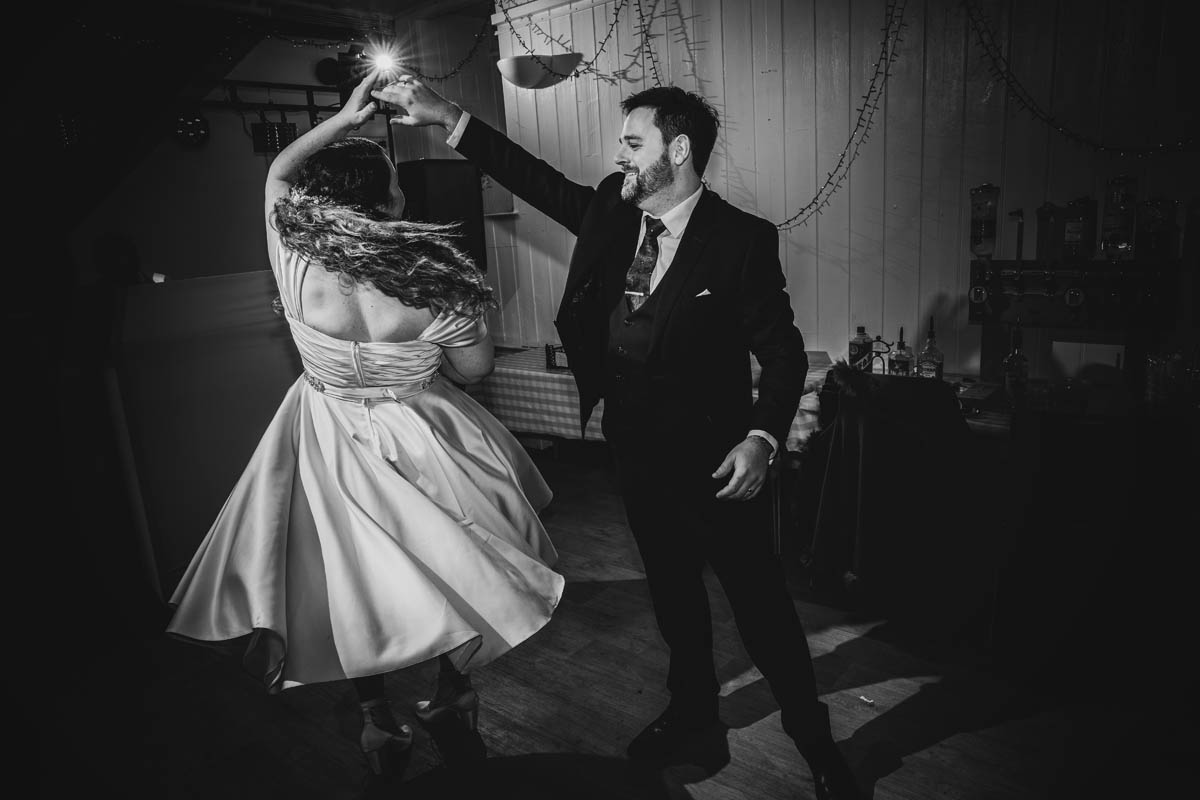 black and white photograph go the groom spinning his wife around, her wedding gown fans out as she spins