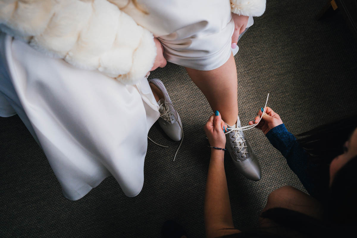 the bride's friend helps her tie up her wedding shoes