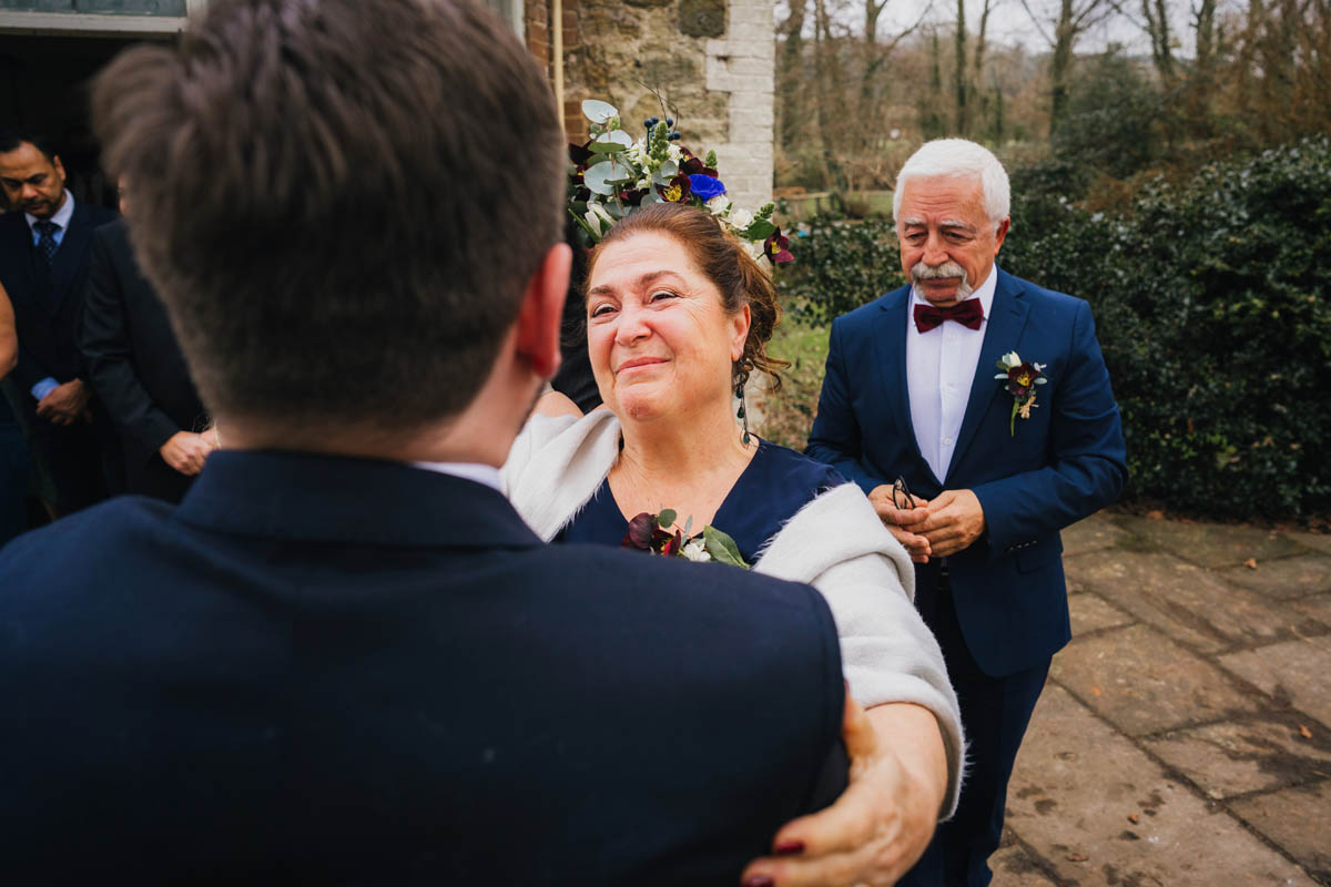 the brides mum grasps her new son-in-law and smiles emotionally as the father of the bride looks on behind