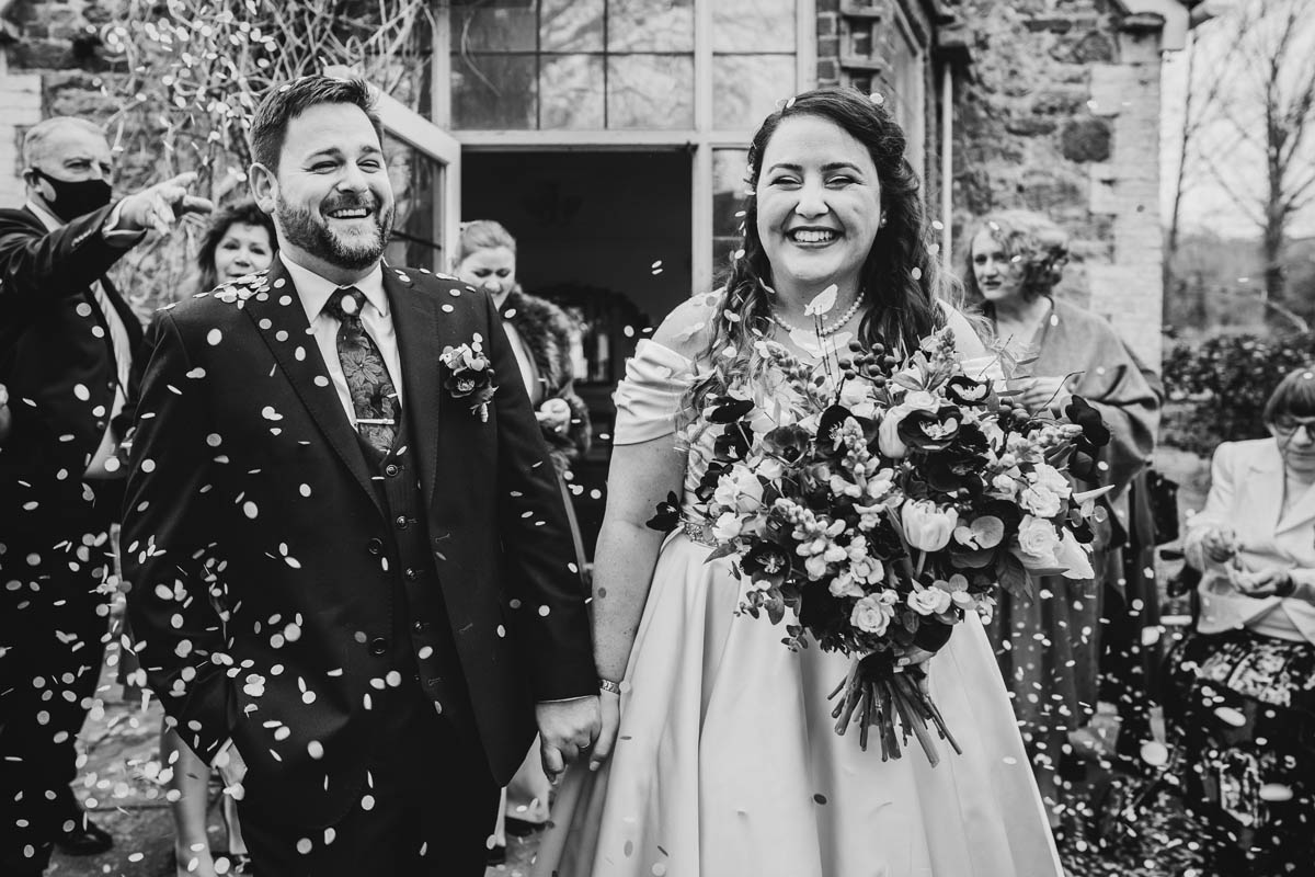 black and white photograph of the newly married couple being covered in confetti, guests throw confetti in the background