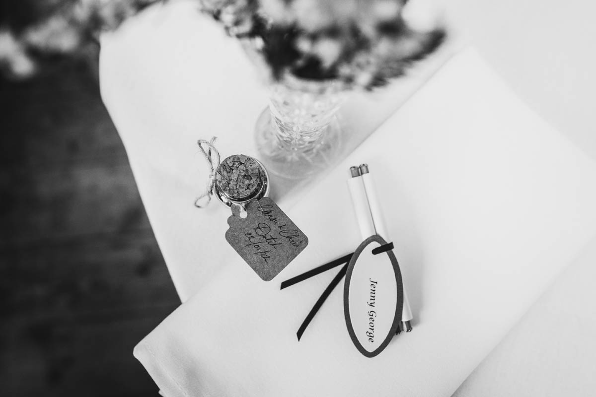black and white photograph of table decorations including a scroll with a wedding guest's name, a wedding favour and a vase of flowers