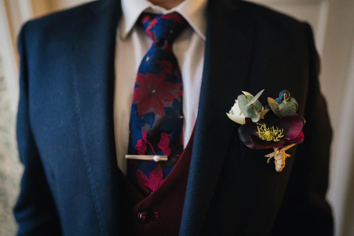 close up of the groom's chest, featuring his tie, tie clip, waistcoat and buttonhole