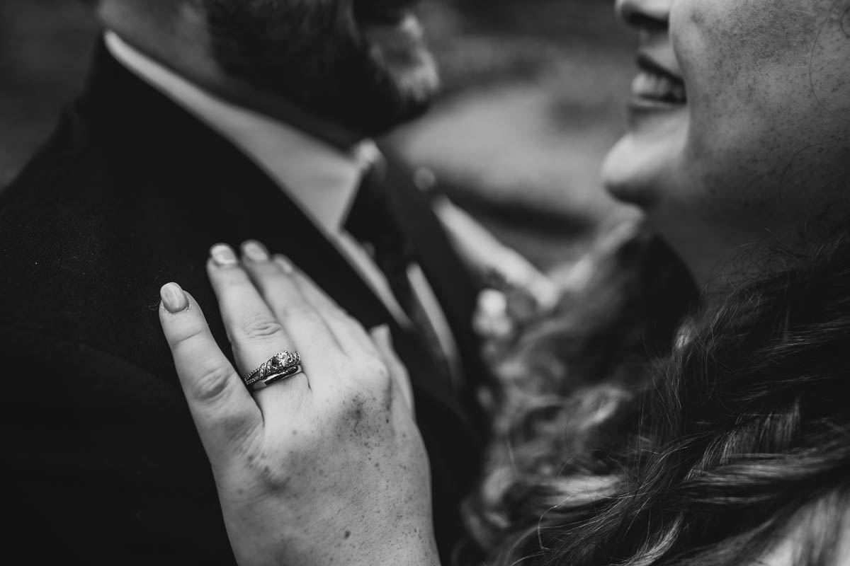 black and white close-up of the bride's wedding and engagement rings. her hand rests on the groom's suit lapel