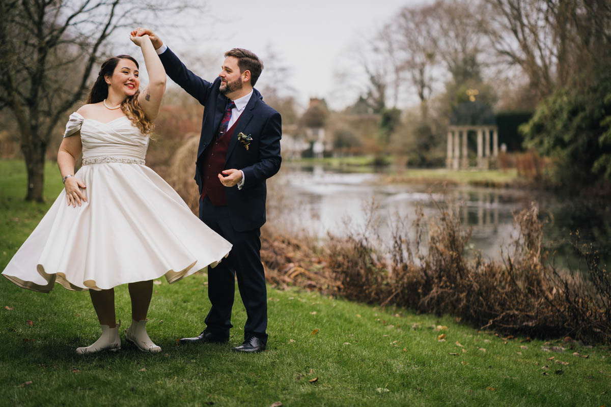 groom spinning his wife around as her tea-length dress fans out in front of the lake at springhead trust