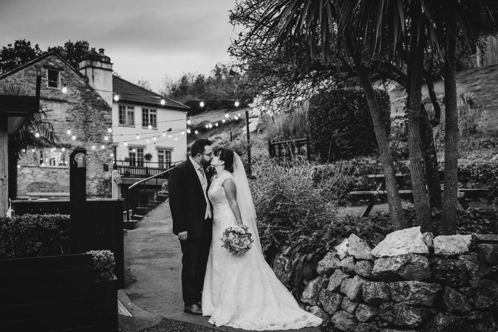 a man in his morning suit kisses his new wife in her bridal gown, she holds her bouquet in one hand. they kiss in front of Bickley mill wedding venue