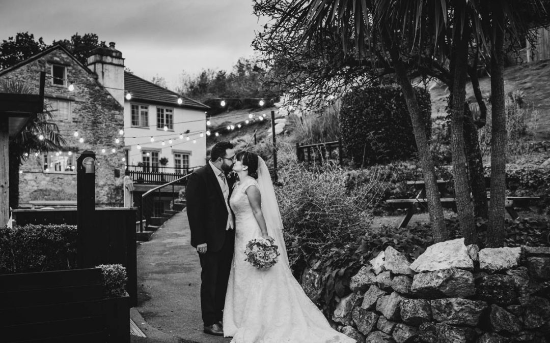 a man in his morning suit kisses his new wife in her bridal gown, she holds her bouquet in one hand. they kiss in front of Bickley mill wedding venue