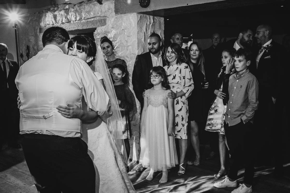 the first dance of the newly married couple and their wedding guests behind smiling and watching