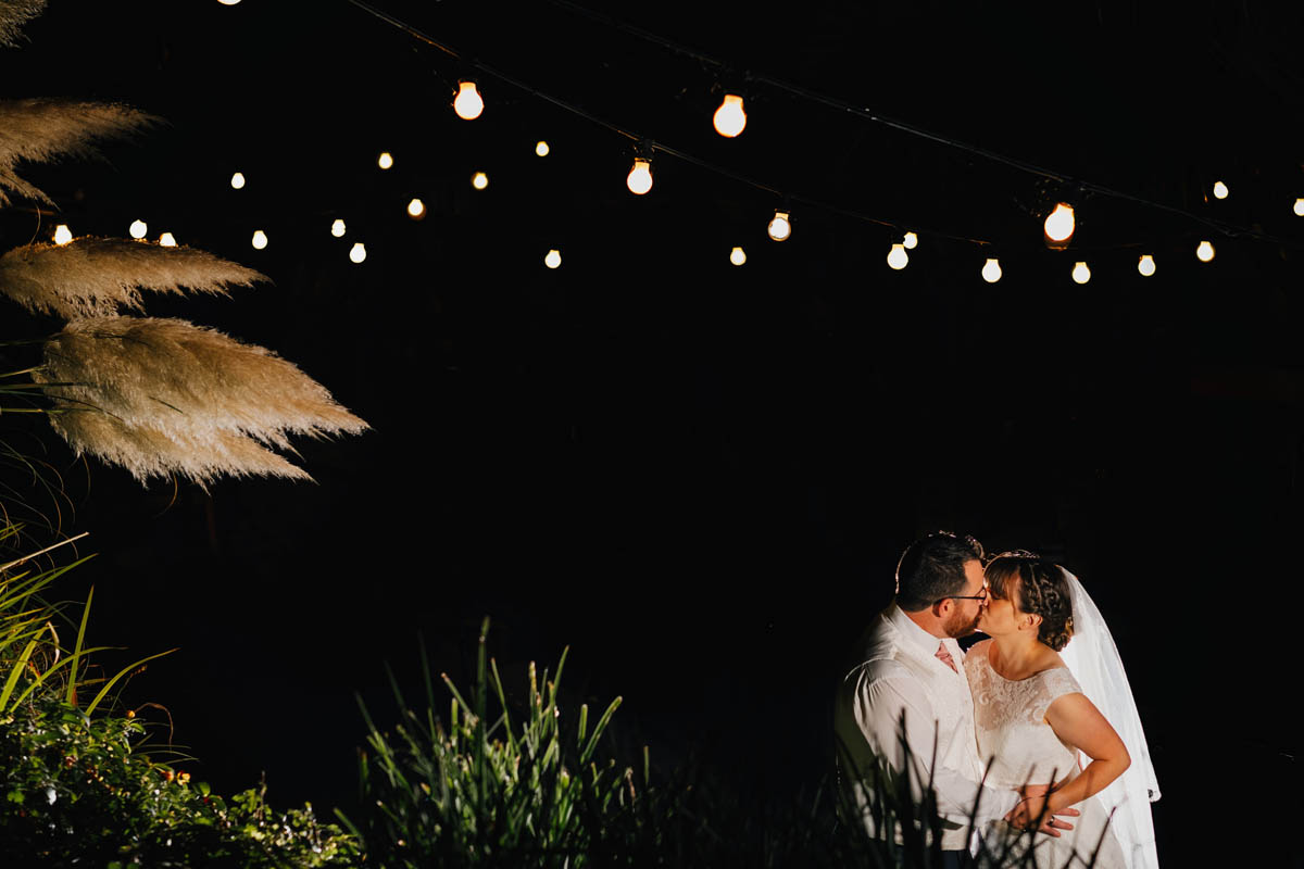 night portrait with off camera flash of a newly married couple kissing under the festoon lights