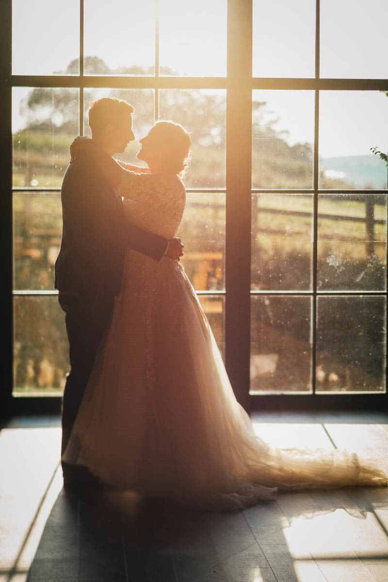 a silhouette of the newlyweds sharing a kiss in the golden hour light with Devon countryside stretching behind them